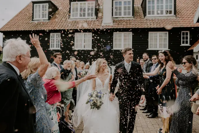 Couple walking towards camera as guests throw confetti