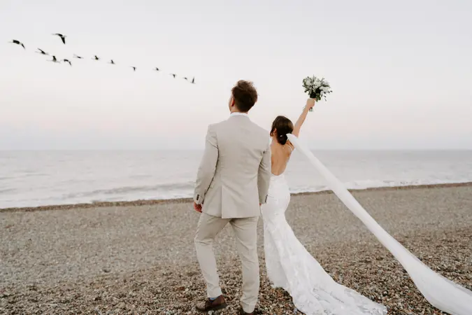 Couple on beach with bride holding bouquet in the air
